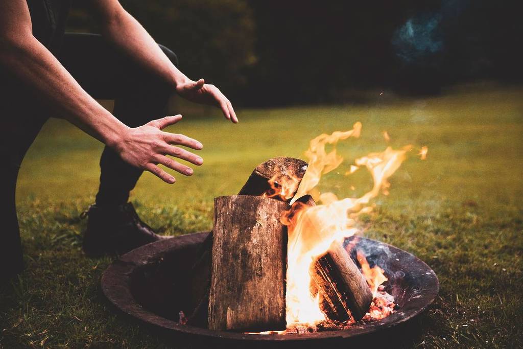 Person warming hands by an open fire pit on the grass at Bellingen Valley Lodge