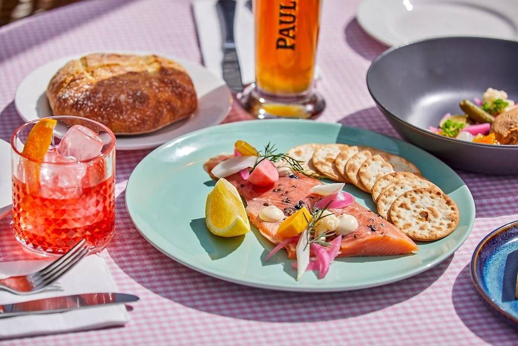 Plate of smoked salmon with crackers, pickled vegetables, and lemon wedges, accompanied by a drink and beer on a checkered tablecloth in a restaurant in Jindabyne nsw