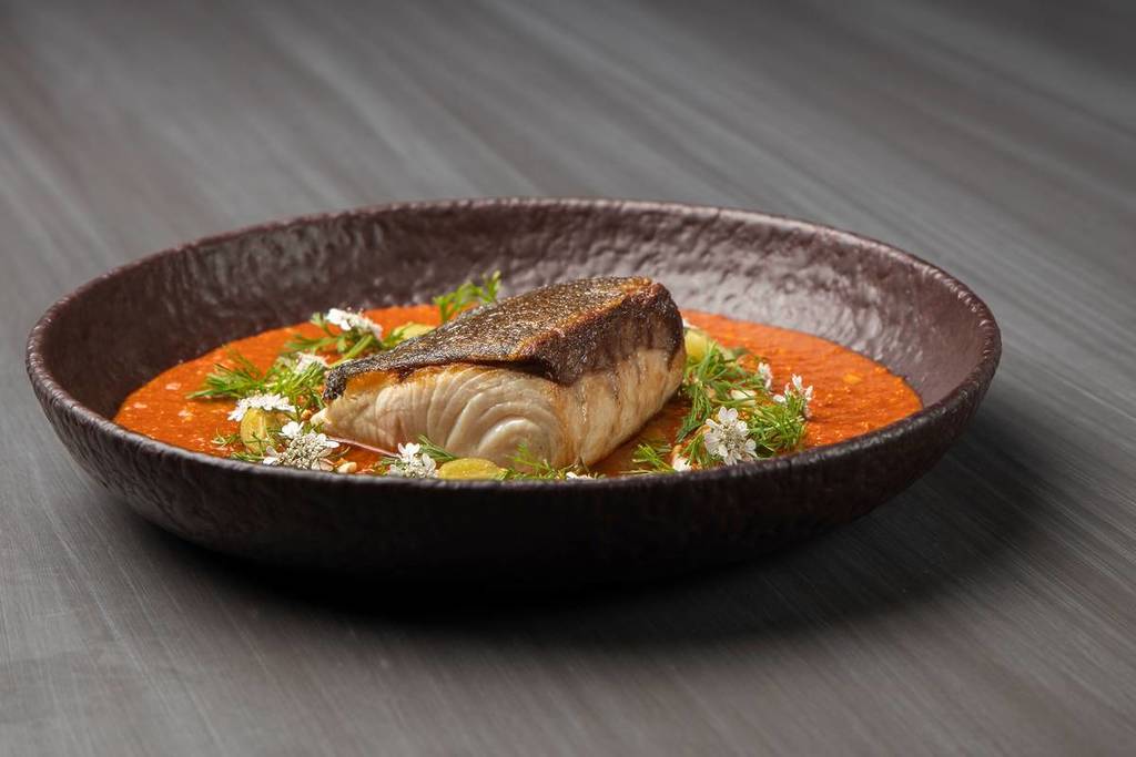 A beautifully plated dish from Paste Australia in Mittagong, featuring seared fish in a rich red curry sauce, topped with fresh herbs and edible flowers