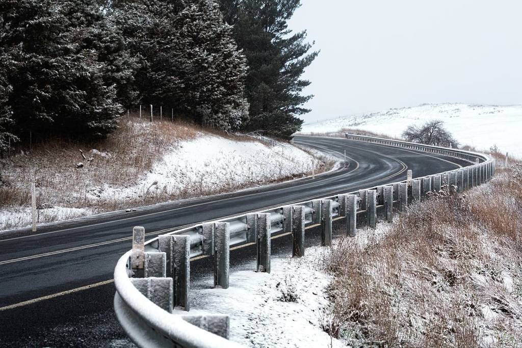 Snow-covered hills with a winding highway cutting through the landscape under a cloudy winter sky in Jindabyne NSW