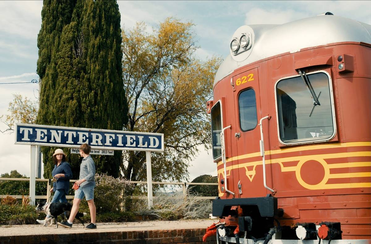 A family walking alongside a vintage train at Tenterfield station, with the train and station sign in the background