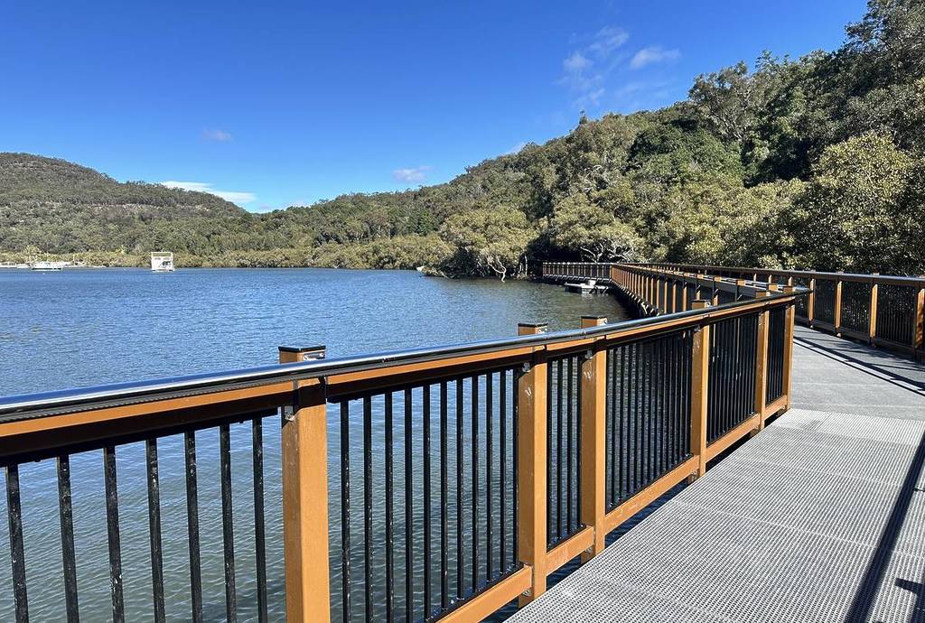 A wide boardwalk stretches along the water at Kangaroo Point in Brooklyn, framed by bushland and clear blue skies on a sunny winter day