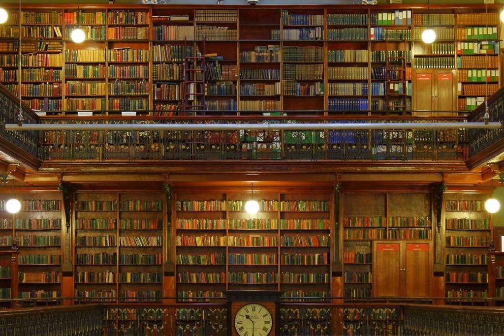Close-up view of the bookshelves inside the Mortlock Chamber at the State Library of South Australia, showing intricate ironwork, warm wooden shelves, and a large central clock beneath rows of vintage books