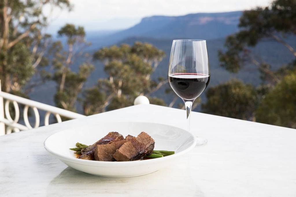 Glass of red wine and a plate of roast beef with mountain views in the Blue Mountains, NSW