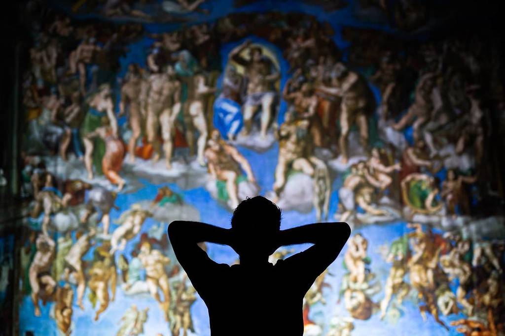 A man stands facing up at one of Michelangelo's frescoes at The Sistine Chapel Exhibition.