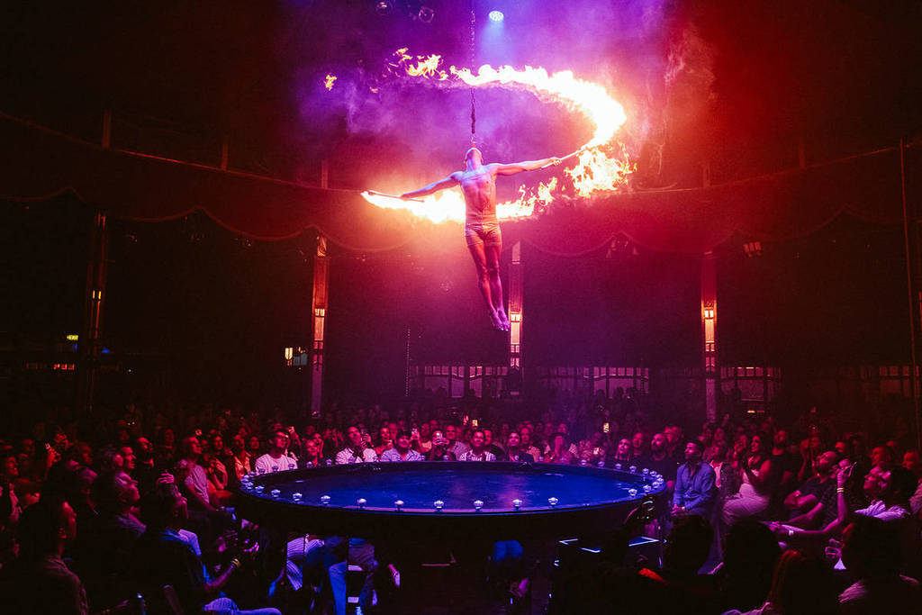 A man hangs from the ceiling and twirls around with fire batons above a crowd at La Ronde.