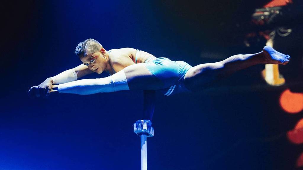 A male performer does the splits whilst balancing on a beam at La Ronde.
