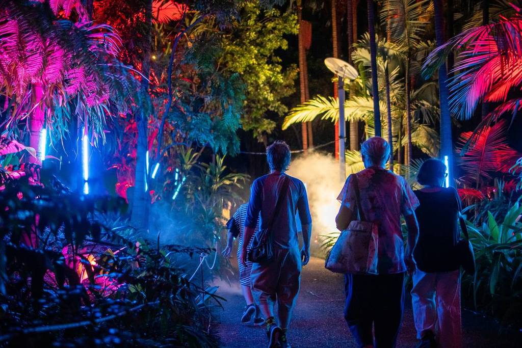 Visitors walk through a neon-lit jungle path at night during the Echoes light and sound experience at Bella Vista Farm