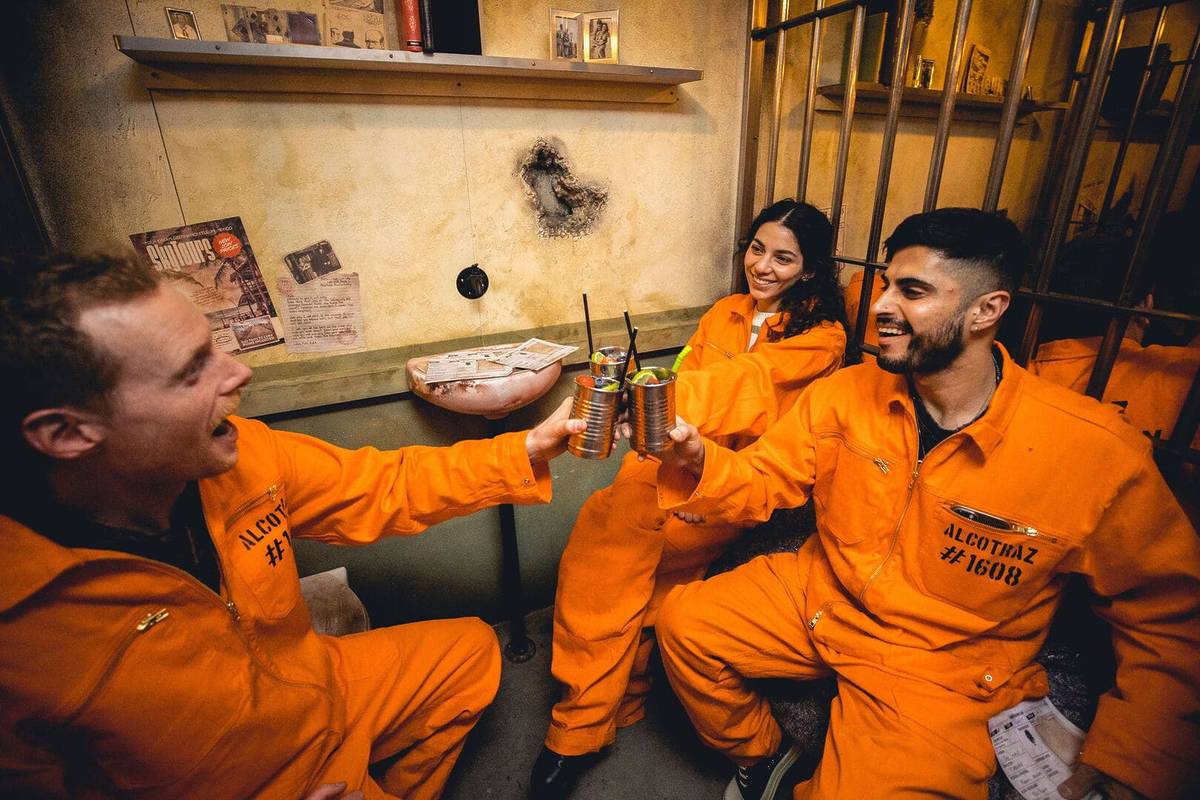 Three friends in orange jumpsuits cheers with a drink in their hands at Alcotraz.