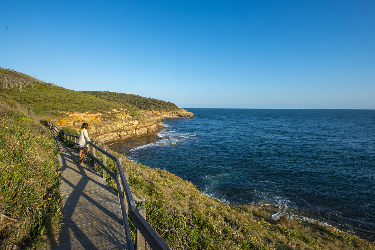 A hiker enjoying the views at the Bouddi Coastal Walk, with the ocean stretching ahead and a clear blue sky in the background