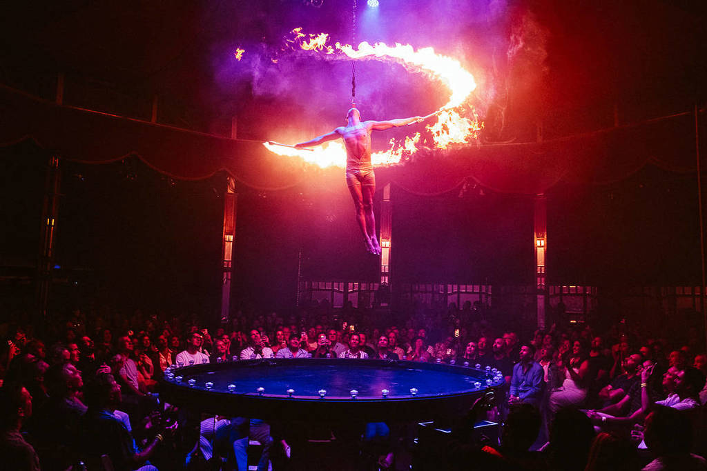 A man hangs from the ceiling and waves around batons lit on fire at La Ronde.