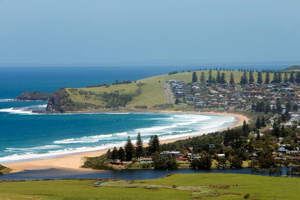 Aerial view of Gerringong with a sandy beach, turquoise waters, and lush green hills in the background