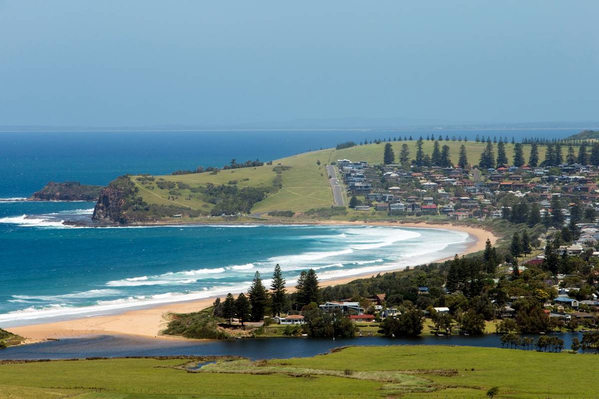 Aerial view of Gerringong with a sandy beach, turquoise waters, and lush green hills in the background