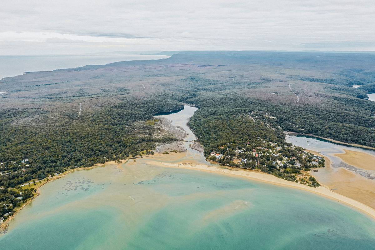 Aerial shot of Bundeena’s picturesque coastline, with lush green forest meeting golden sands and clear waters