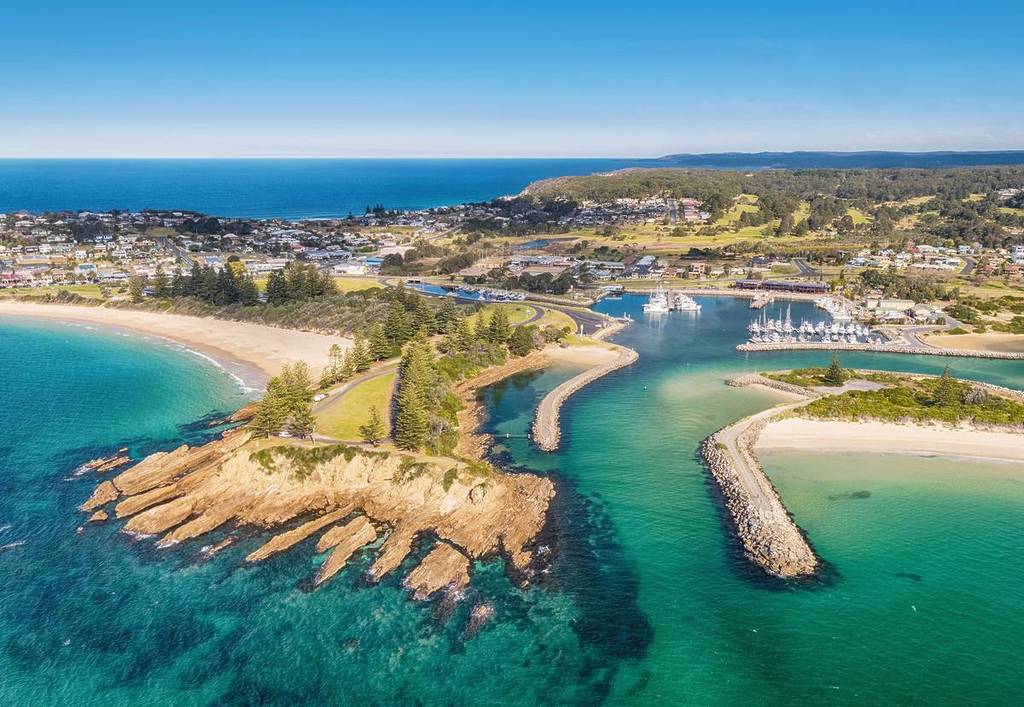 Aerial view of Bermagui, NSW, showcasing its stunning coastline with turquoise waters, a peaceful marina, and scenic beaches