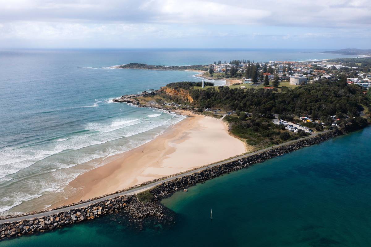 A scenic view of Yamba main beach with a rocky coastline, a lighthouse, and a coastal town nestled along the shore