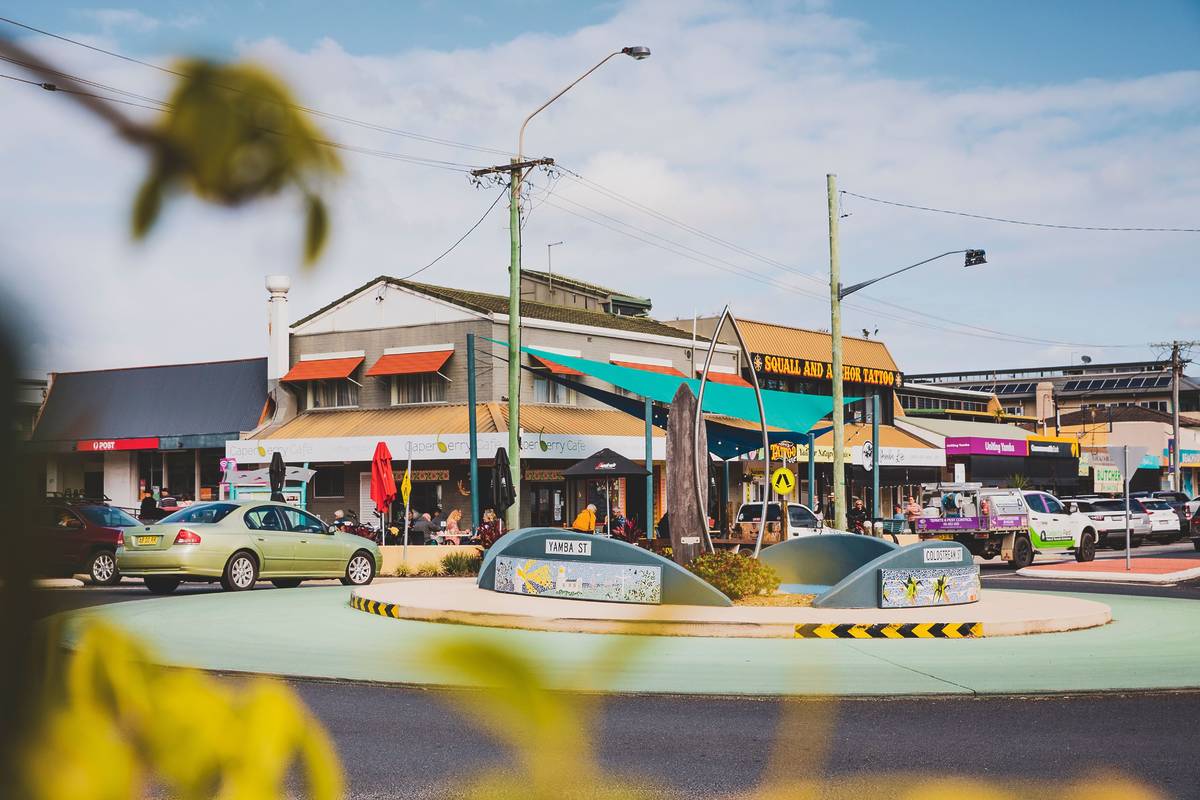 A vibrant street view of Yamba’s town center, with cafes, shops, and a roundabout featuring a local art display