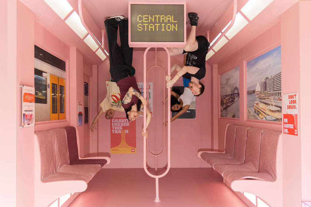 Four friends take a photo in an upside-down train recreation at Mind Games: Art Alive!