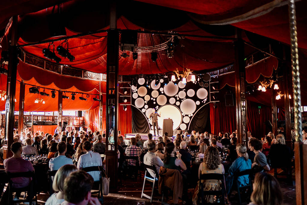 Attendees sit around tables sipping wine while watching Merrick Watt's perform his comedy show, An Idiot's Guide to Wine.