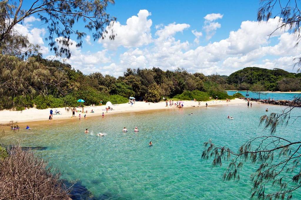 Peaceful beach scene at Brunswick Heads, one of the best alternatives to Byron Bay, featuring clear turquoise water and swimmers enjoying the shallow bay
