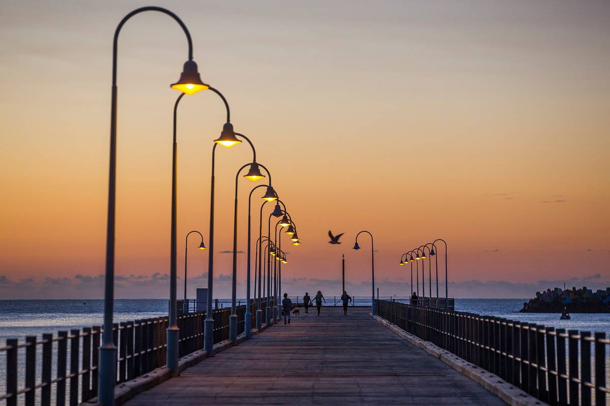 A long pier extending into the ocean at sunset, with streetlights casting a warm glow at Jetty Beach, Coffs Harbour