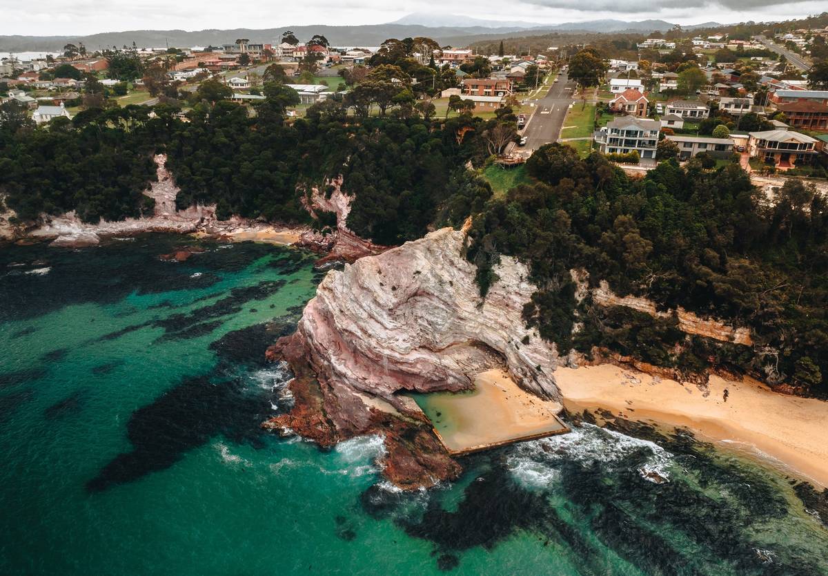 Aerial view of Aslings Beach Rock Pool in Eden, framed by dramatic pink and white cliffs, with the town visible in the background
