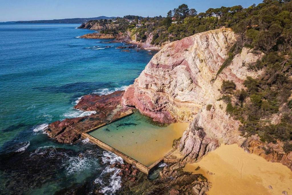 Aerial shot of Aslings Beach Rock Pool, surrounded by vibrant pink cliffs and clear blue-green waters