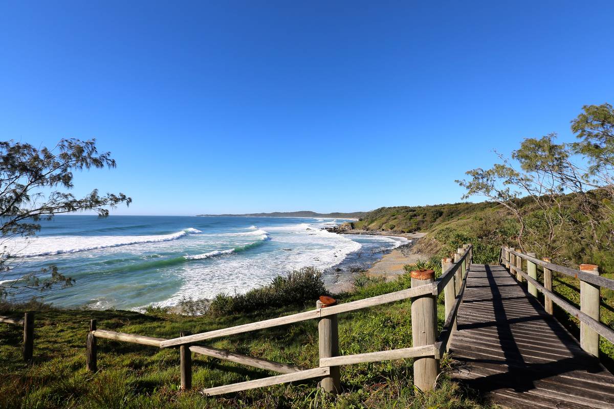 A wooden boardwalk at Minnie Water leading down to the coastline, overlooking rolling waves, and clear blue water
