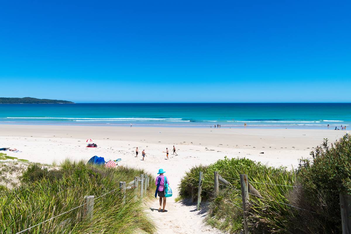 Visitors walking along the white sand at Murrays Beach in Booderee National Park, Jervis Bay, with calm turquoise water and clear summer skies