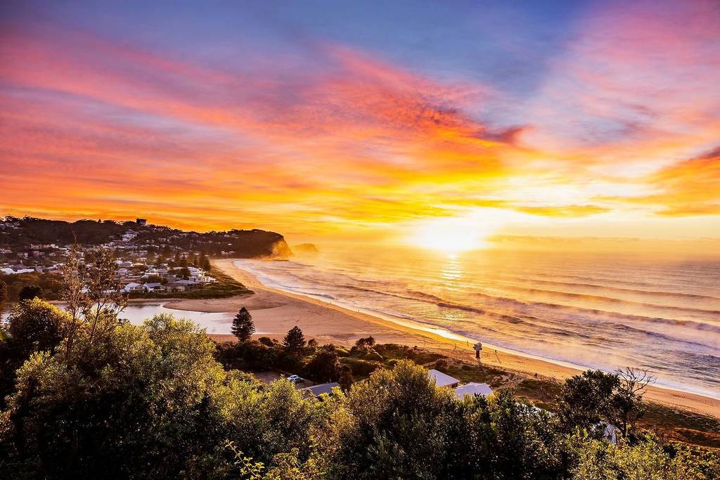 Panoramic view of Avoca Beach at sunset, with golden skies and waves rolling in along the coast