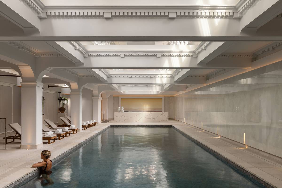 Guest relaxing by the indoor pool at Capella Sydney, featuring white arches, skylights, and elegant lounge chairs