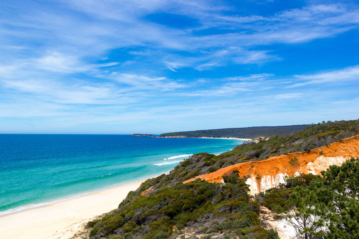 Sweeping coastline near Eden on the Sapphire Coast, with red cliffs, white sand and bright turquoise sea