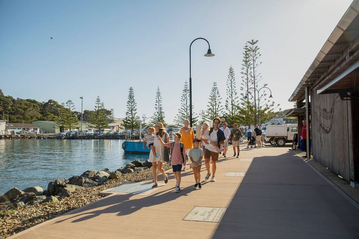 Visitors walking along the Snug Cove waterfront in Eden, with boats and cafes lining the harbour