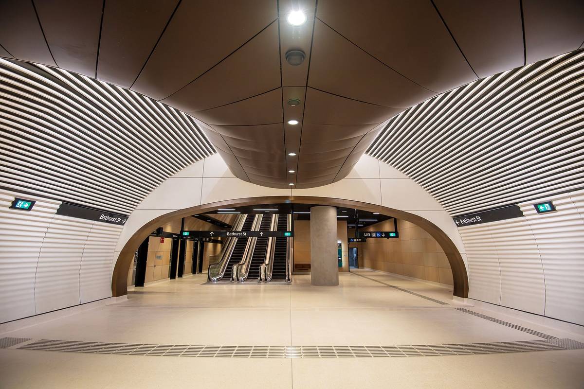 Modern interior of a Gadigal metro station in Sydney with curved metal panels, escalators, and Bathurst Street signage