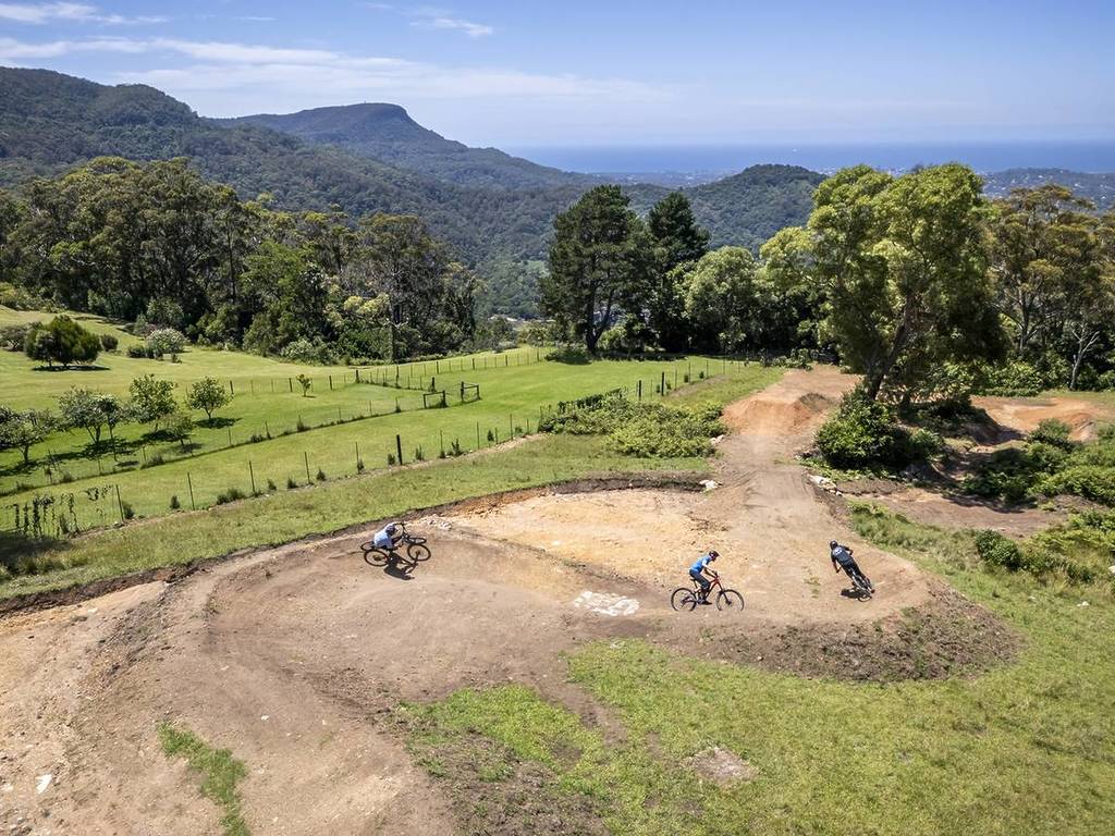 Cyclists navigating the Kembla Mountain Bike Trails with sweeping views of the Illawarra Escarpment and the ocean in the distance