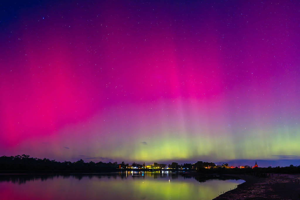 Pink, purple and green Aurora Australis illuminating the night sky and reflecting across a calm lake