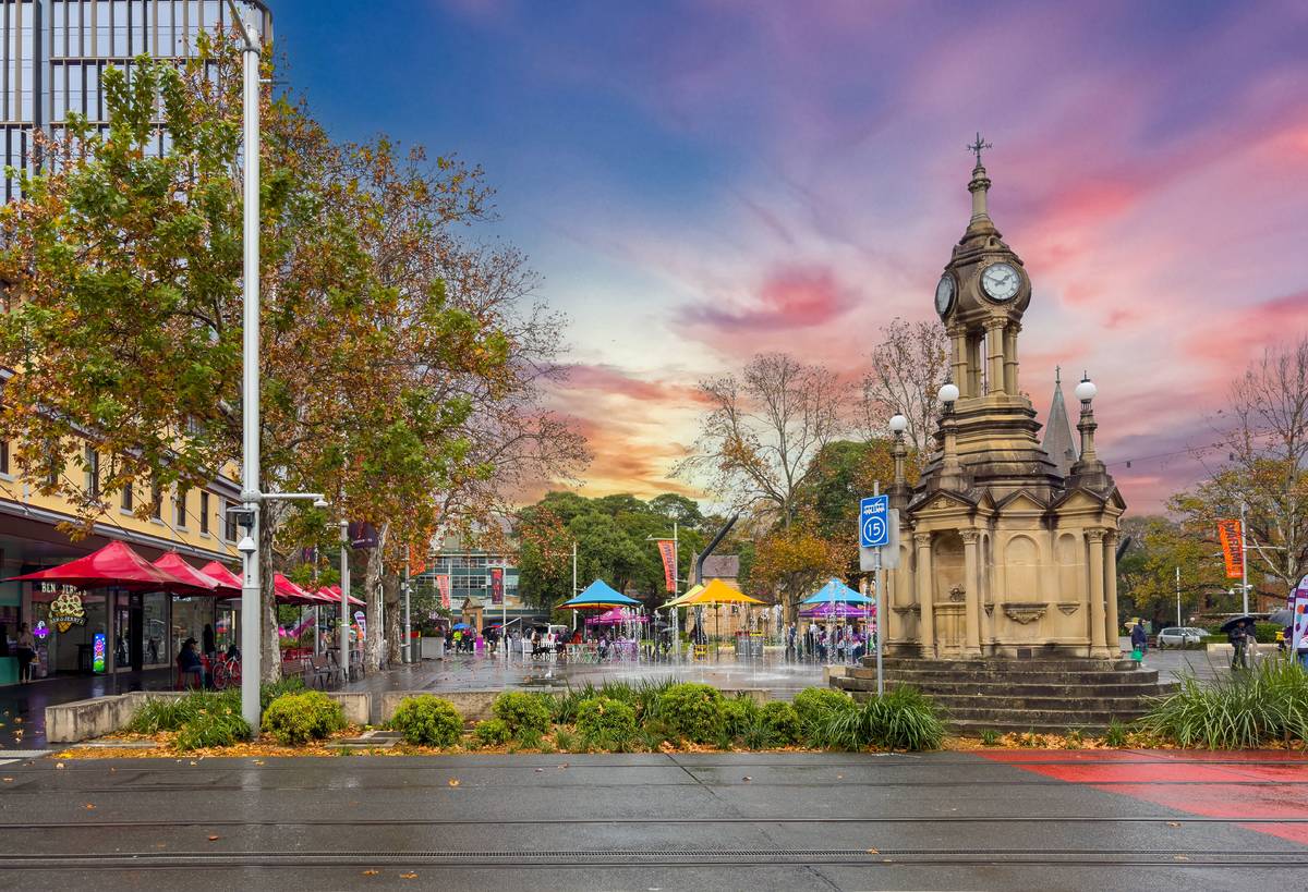 Centenary Square in Parramatta at sunset, with the historic clock tower, colourful market stalls, and people walking near the fountains