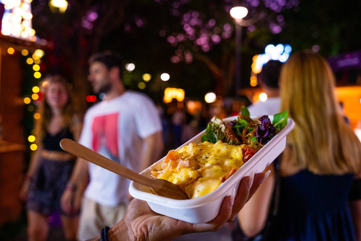 Close-up of a festive street food dish held up at a Christmas market in Sydney, with people and lights in the background
