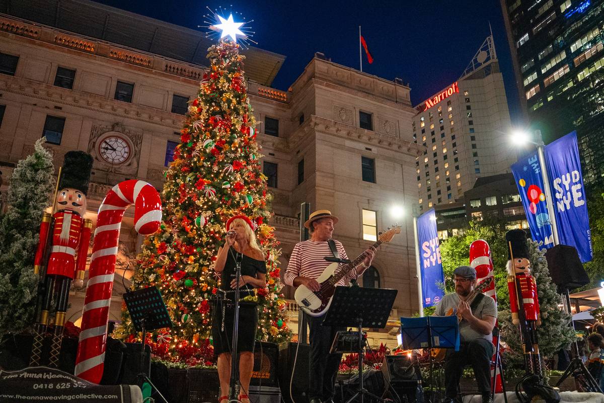 Live band performing Christmas music beside a decorated tree and giant candy canes at Sydney's Jolly Market in Circular Quay