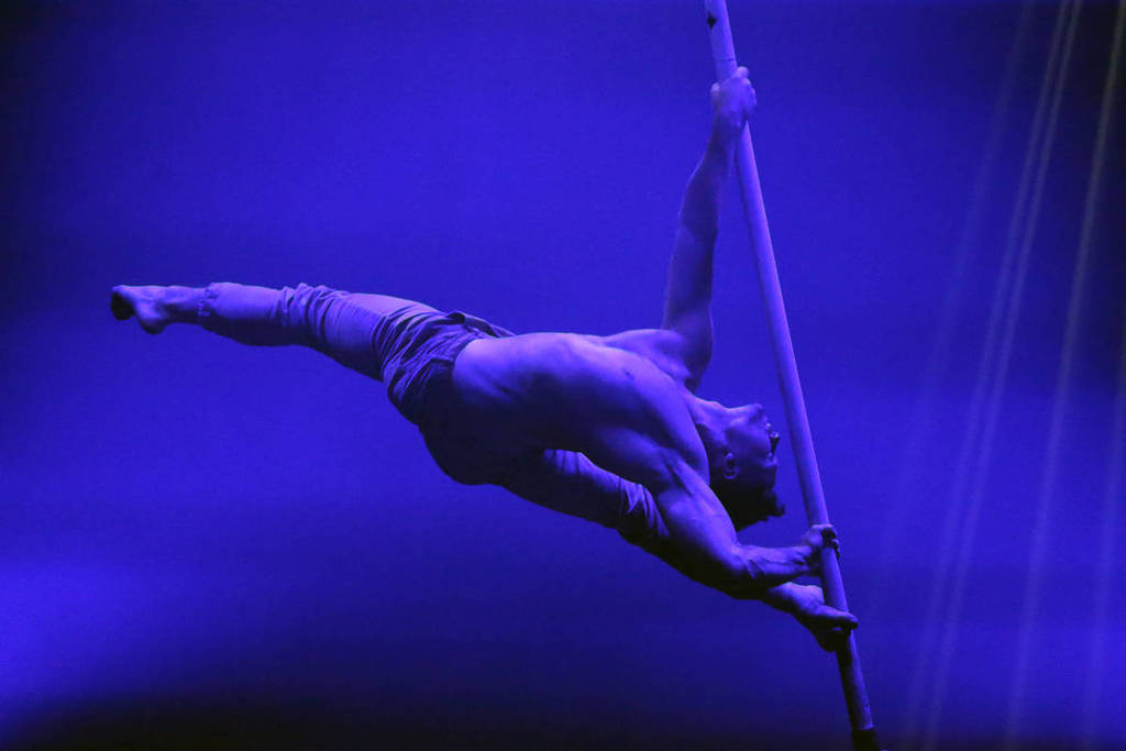 A man does the splits in the air, supporting his body by holding a rope dangling from the ceiling.