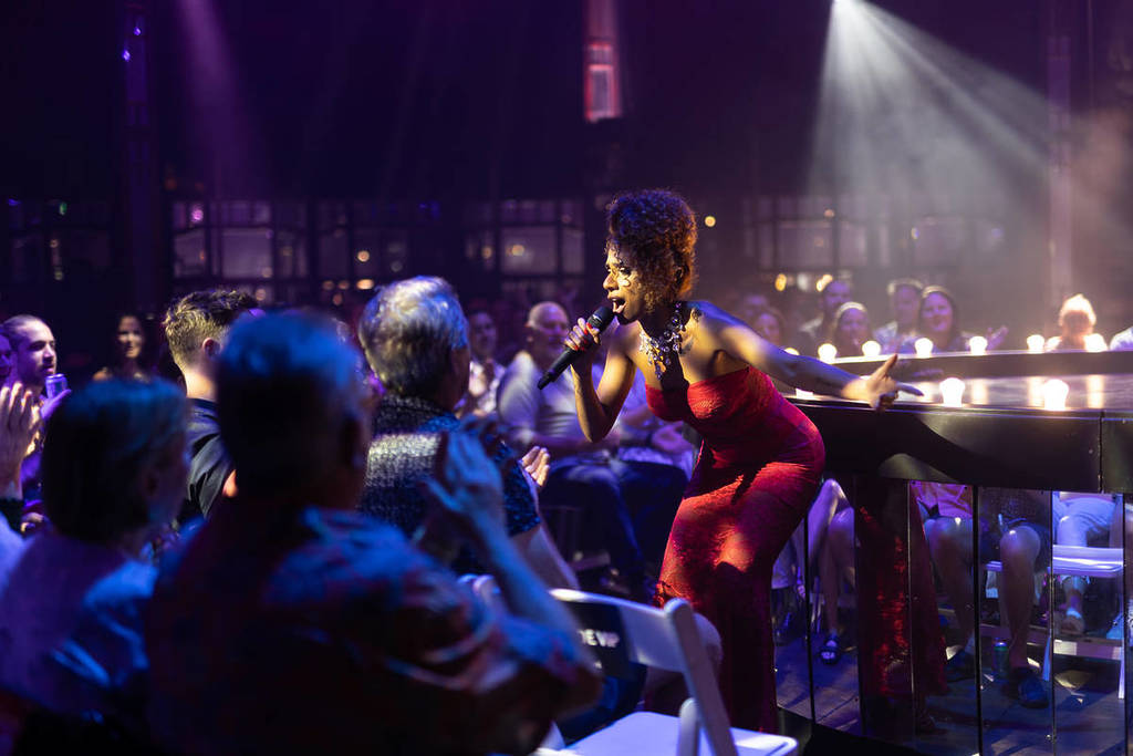 A woman in a red dress stands amongst the crowd at La Ronde, singing into the microphone.