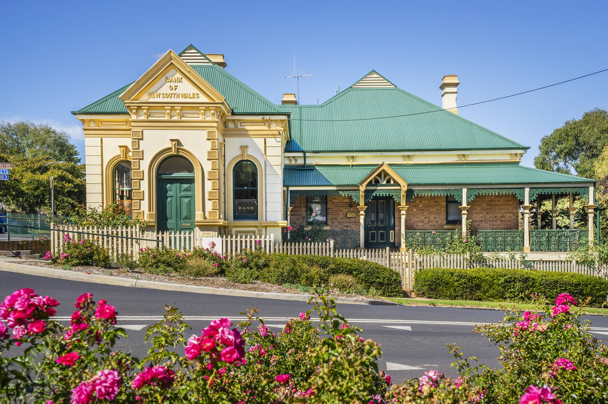 Heritage Bank of NSW building in Millthorpe, one of the best fairytale small towns in NSW, framed by vibrant pink roses and a picturesque white picket fence