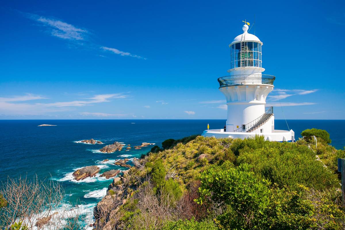 White lighthouse perched on a rocky headland above deep-blue ocean at Seal Rocks in the Pacific Palms region