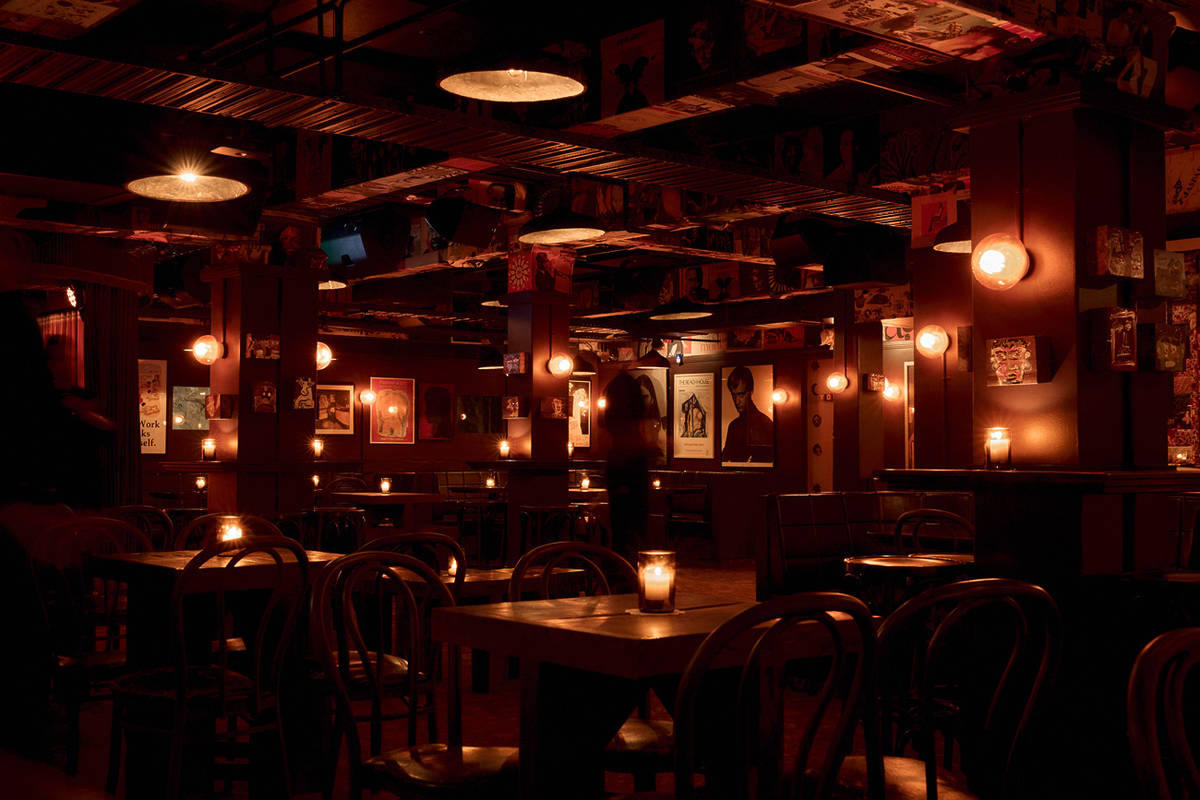 The candlelit interior of Curtains Jazz Club in Sydney, with low tables, bentwood chairs and vintage posters lining the room