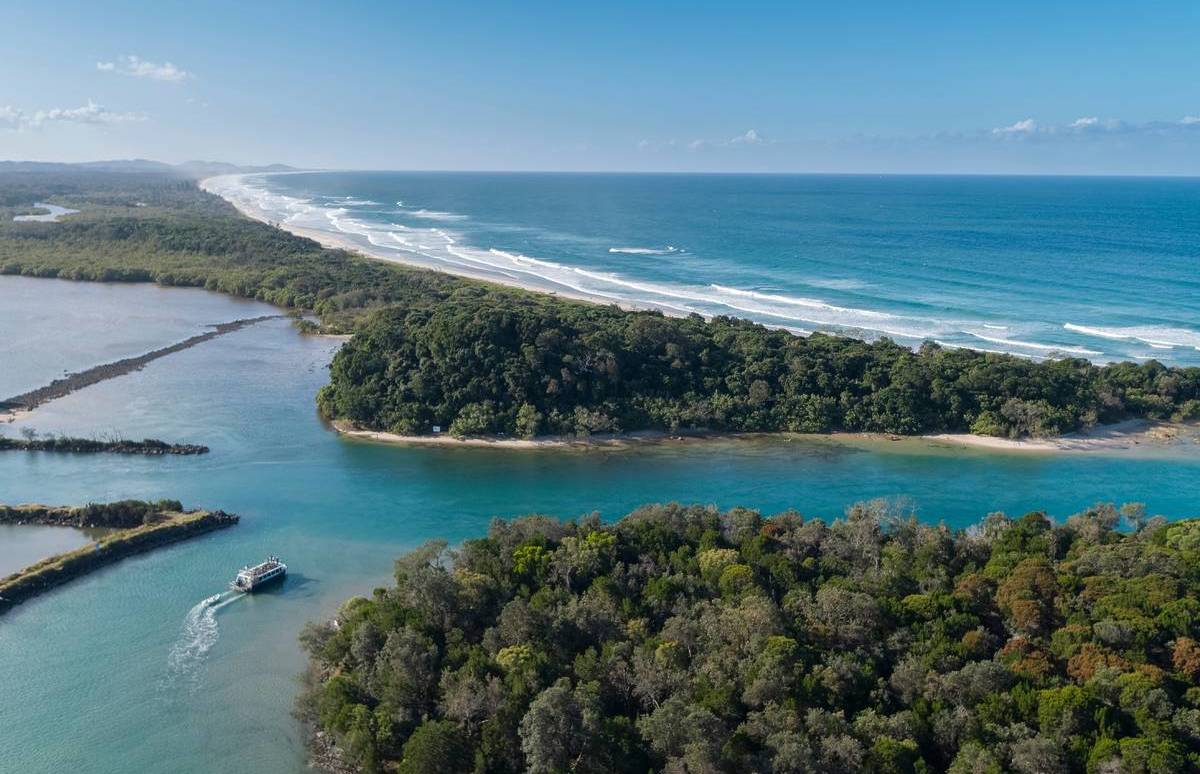 Aerial view of the Brunswick River winding through dense bushland before opening out to the ocean