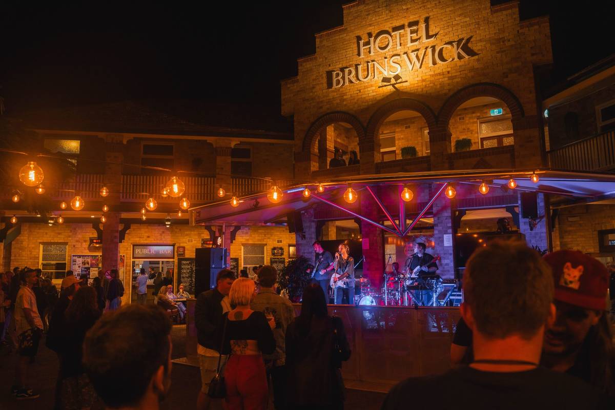 Crowd gathered in the beer garden at Hotel Brunswick as a live band performs under warm string lights at night