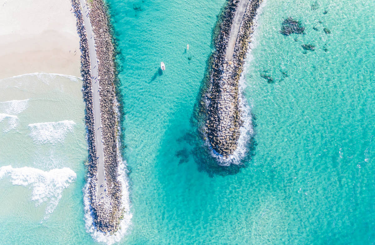 Drone view of the Brunswick Heads breakwalls separating the river from the ocean with bright turquoise water on both sides