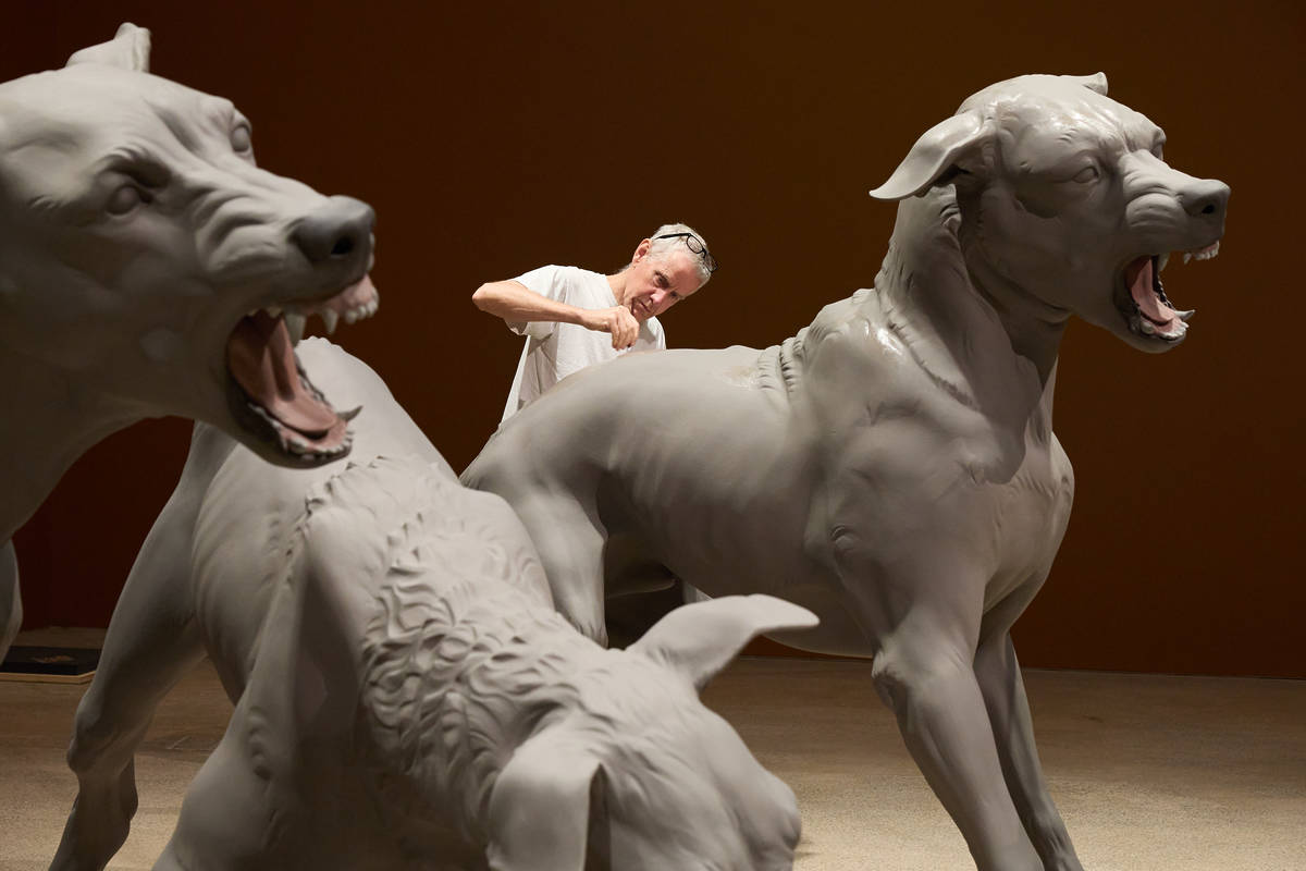 A man works between two large, hyperreal sculptures of snarling dogs in a gallery space