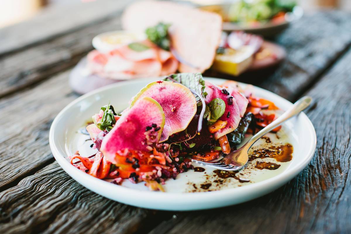 Colourful plated dish with sliced radishes, salad and sauce served on a rustic wooden table in a cafe in Byron Bay