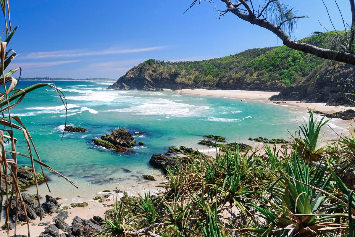 Turquoise waves rolling into a secluded beach in Byron Bay, framed by rocky headlands and coastal greenery